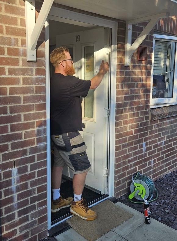 A man is kneeling down to fix a door lock.
