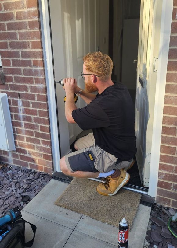 A man is kneeling down to fix a door lock.
