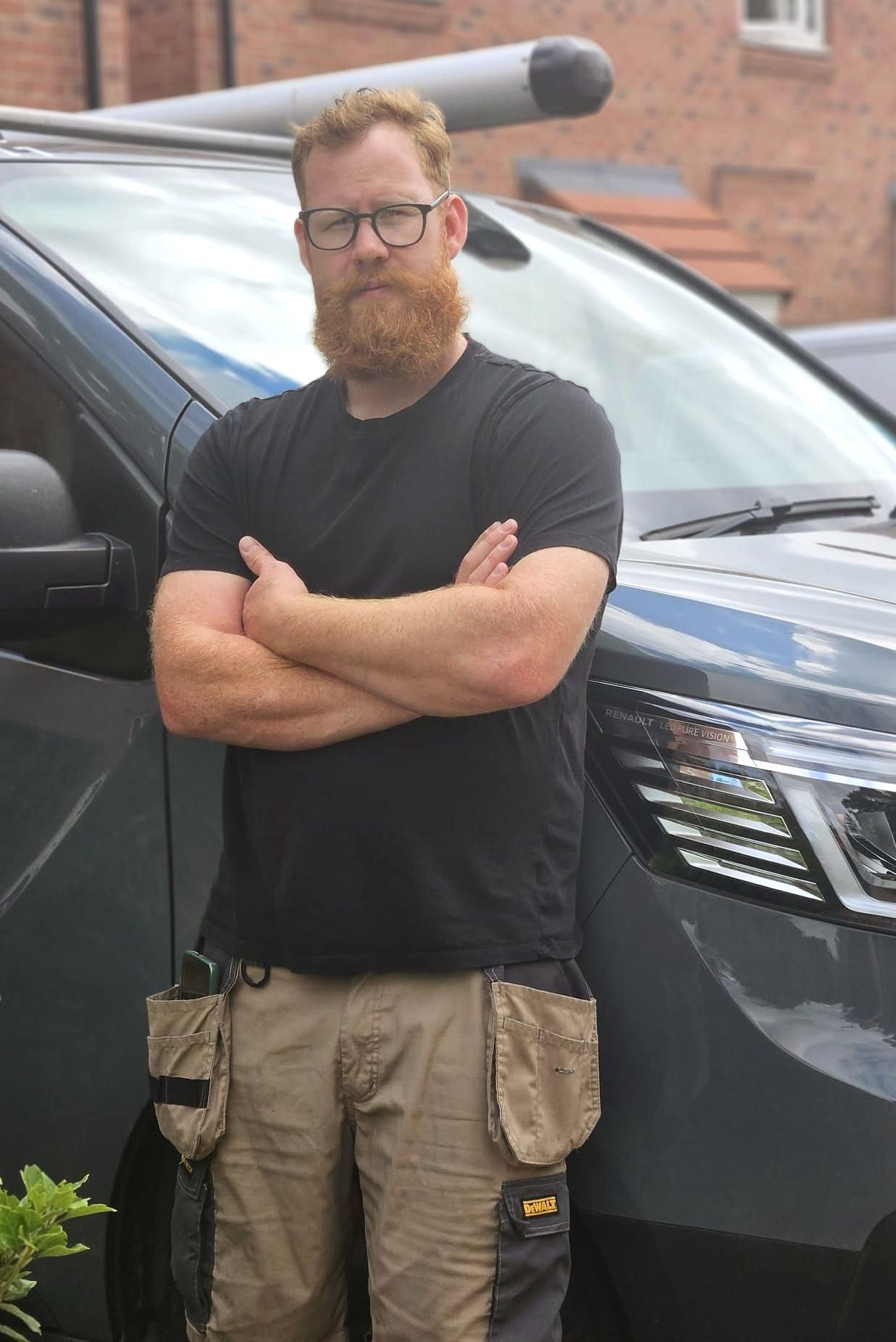 A man with a beard and glasses is standing in front of a van with his arms crossed.