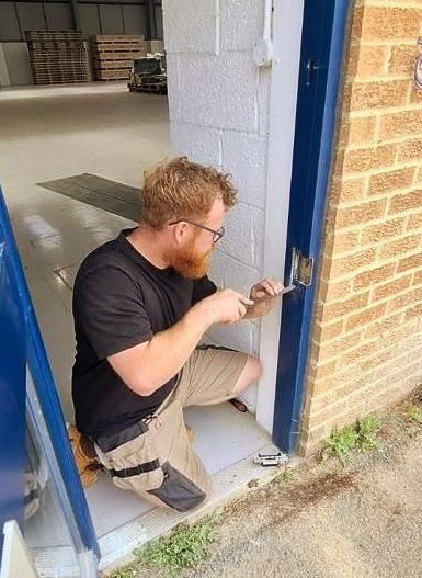 A man is kneeling down to fix a door lock.