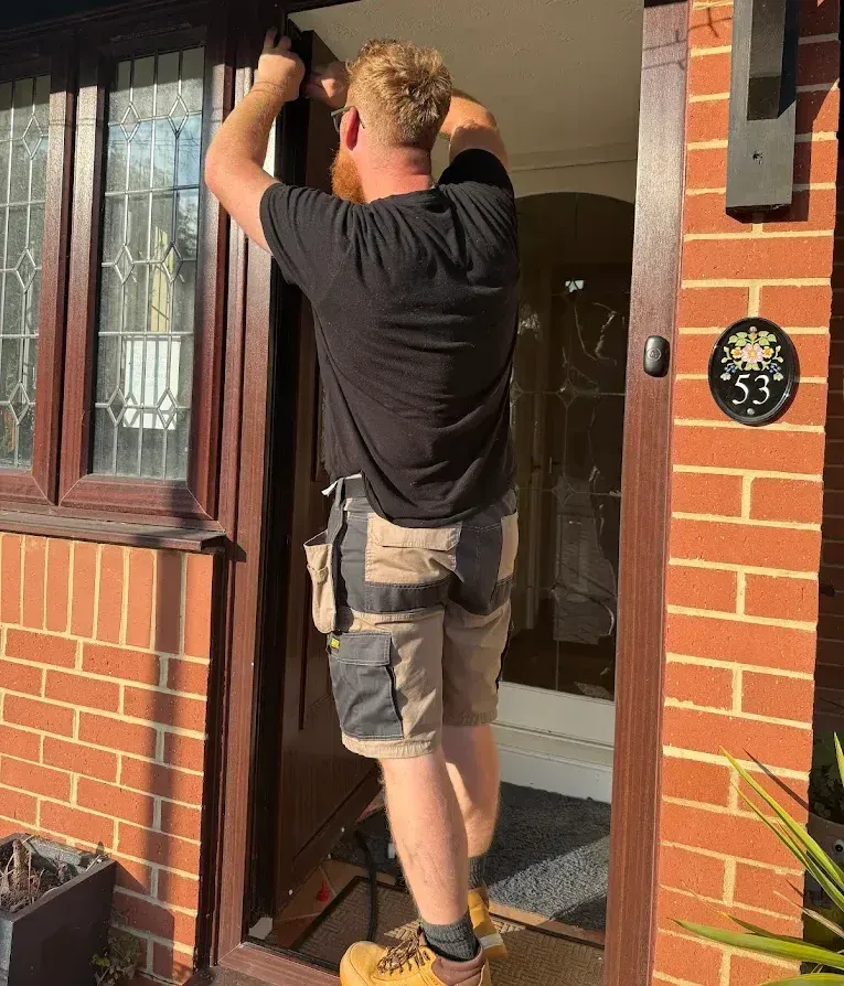 A man is kneeling down to fix a door lock.