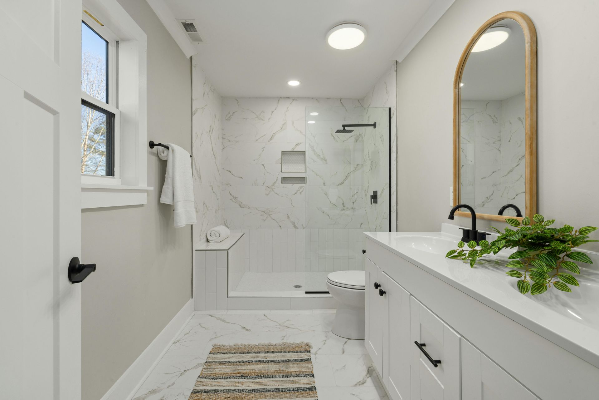 Bright white modern bathroom with walk-in shower, double vanity, and gold-framed mirror