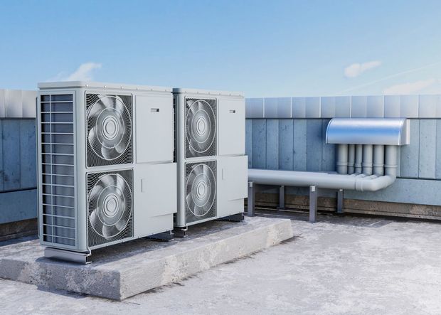 Two air conditioning units on a rooftop, next to pipes and against a blue sky.