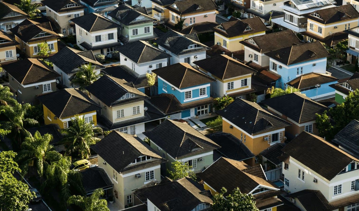 Aerial view of a dense residential neighborhood featuring many detached houses with dark roofs and light-colored walls.
