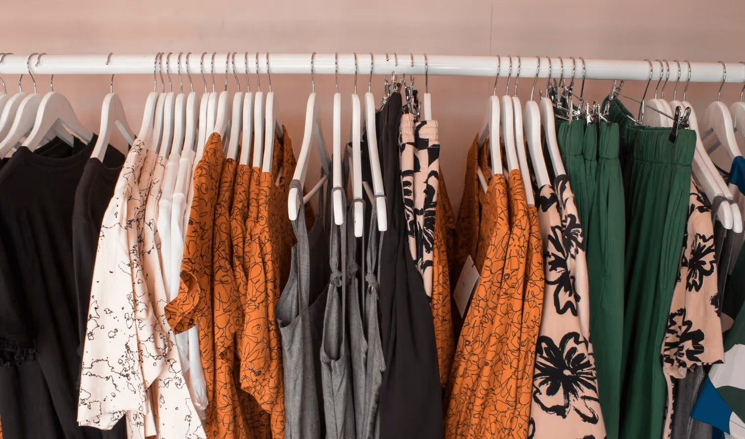 A clothing rack holding a variety of shirts, blouses, and trousers in shades of black, white, orange, and green.