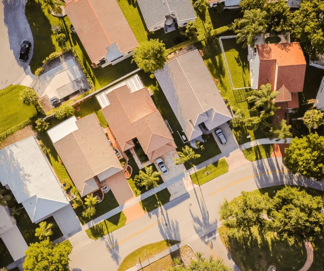 An aerial view of a suburban neighborhood showing multiple single-family homes, driveways, and surrounding greenery.