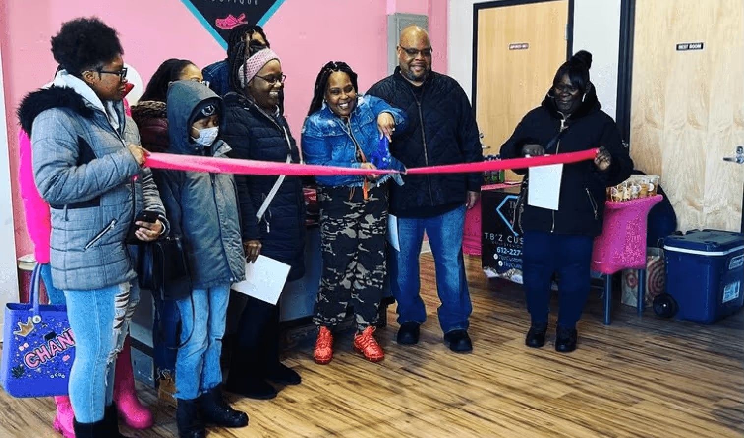 A group of people standing in a line holding a pink ribbon, celebrating a grand opening in an indoor space.