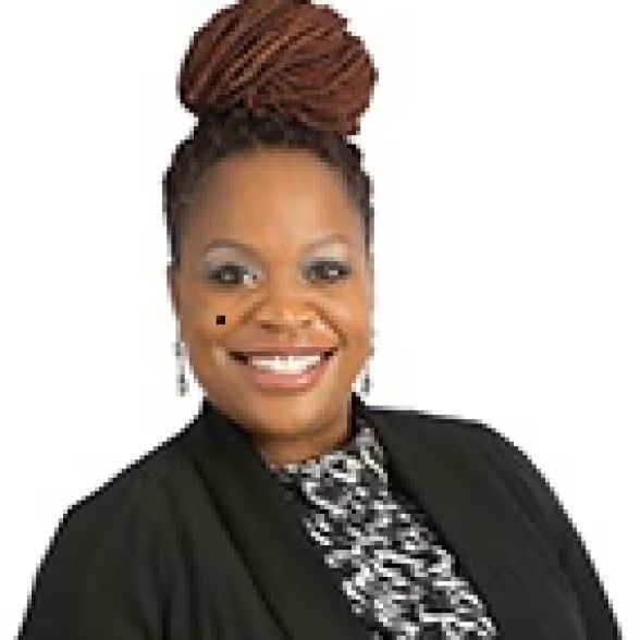 A smiling person with auburn hair in a high bun, wearing a black blazer over a patterned top, set against a white background.