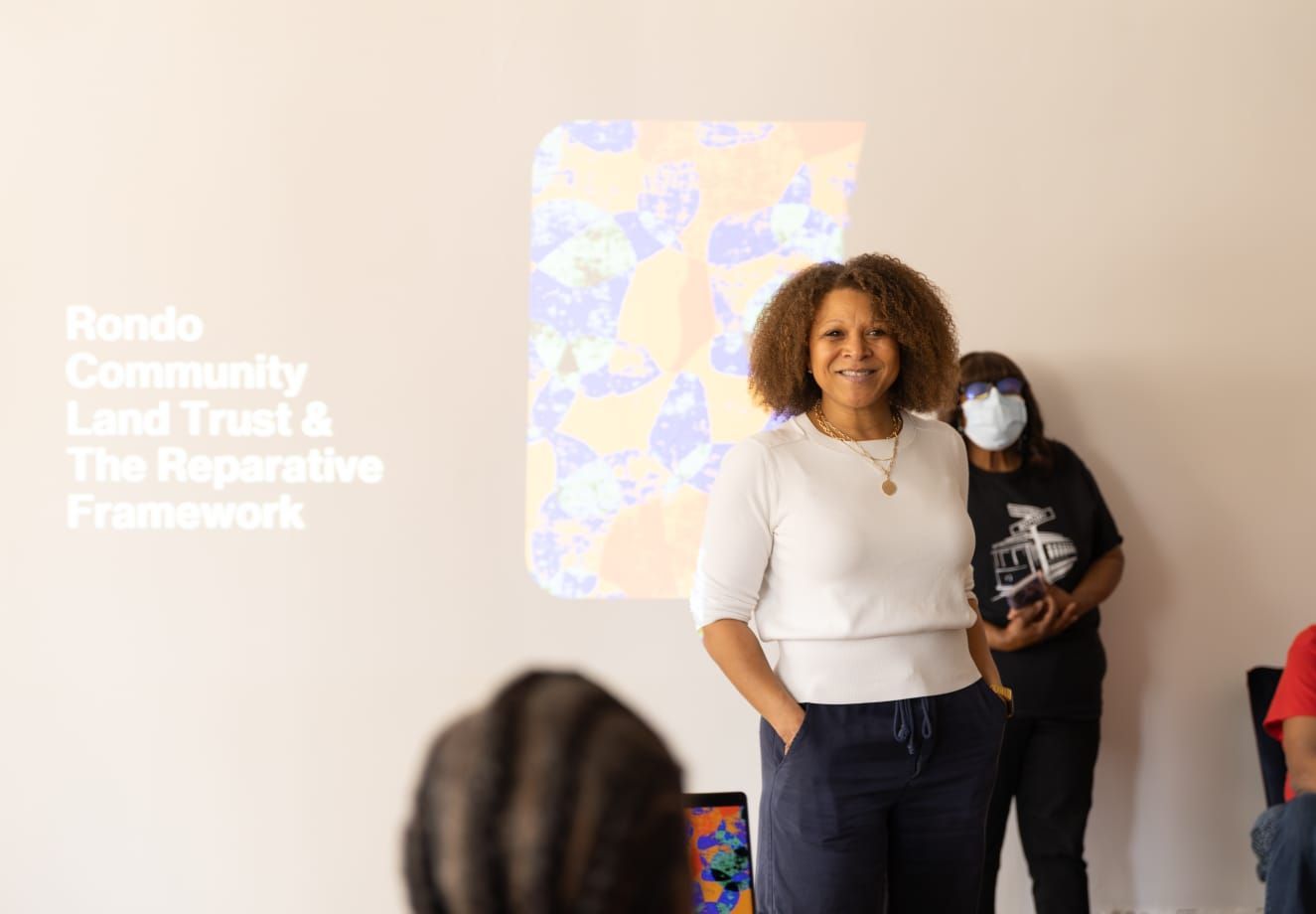 A speaker stands before a wall projection titled 