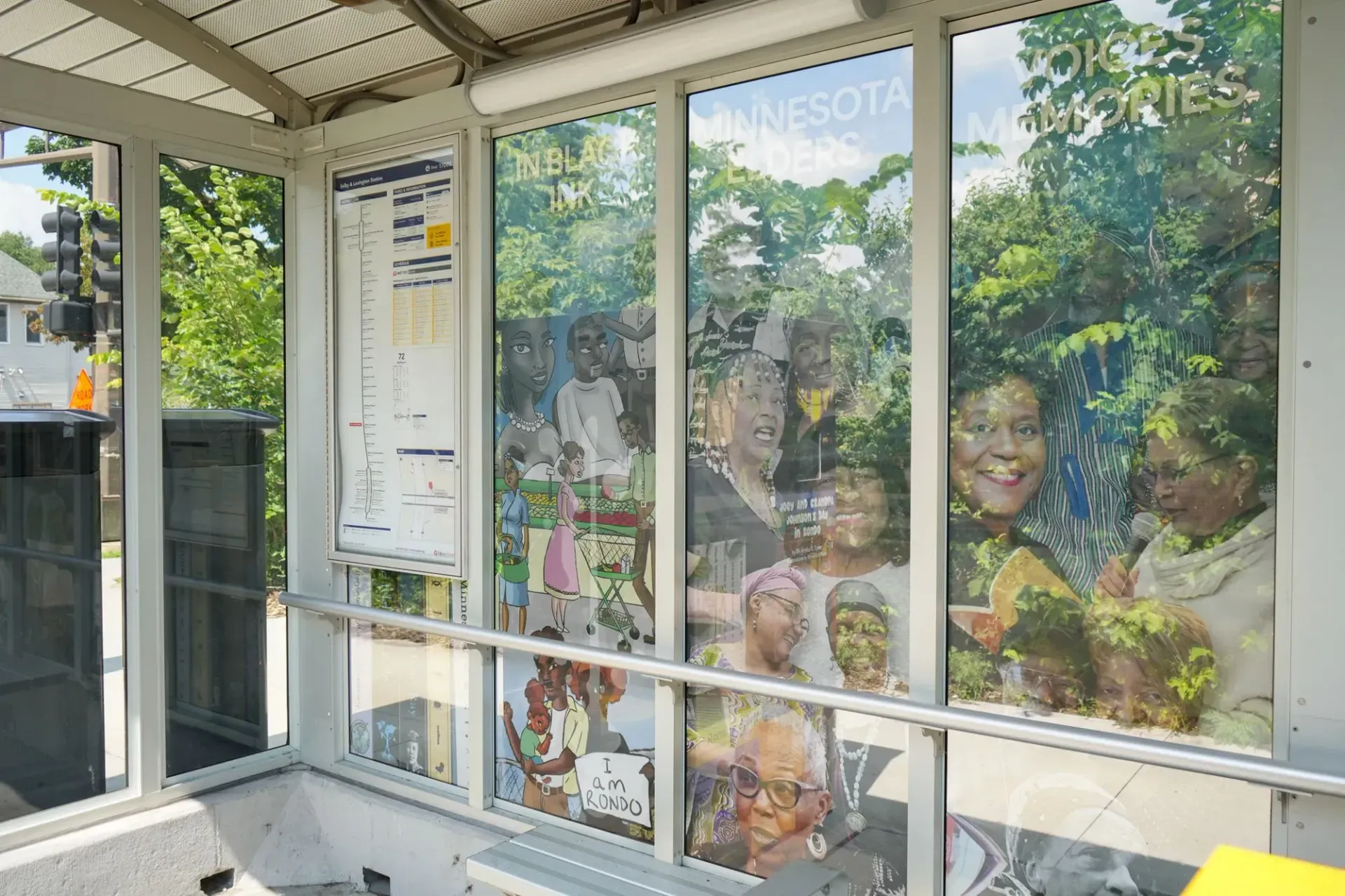 A bus shelter with a glass wall featuring a photographic collage of people's faces and a transit route map.