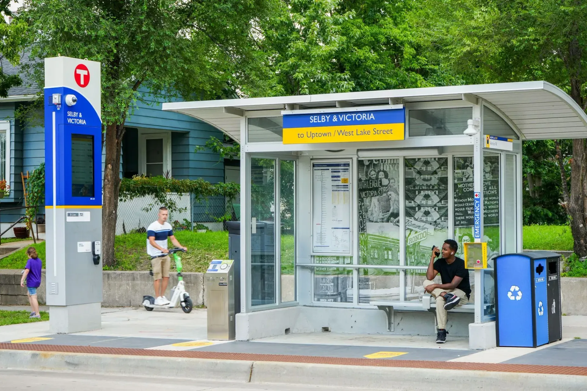 A bus stop with a digital display, a rider on an electric scooter, and a person sitting on the bench.