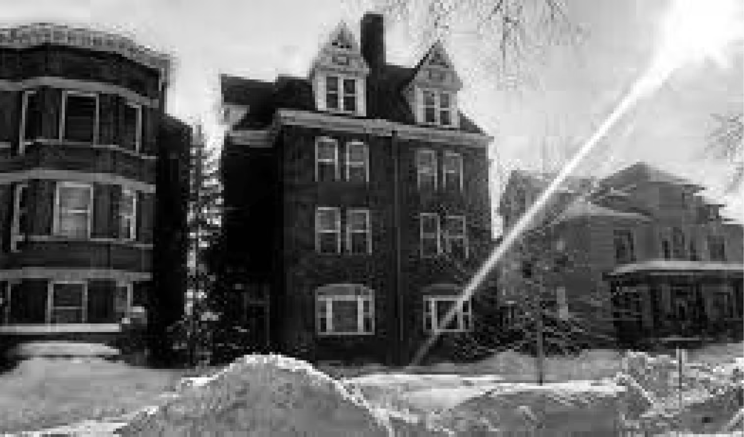 A row of three historic multi-story brick residential buildings covered in snow under a bright, overcast sky.