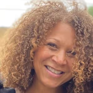 A smiling person with curly, light brown hair looking toward the camera.