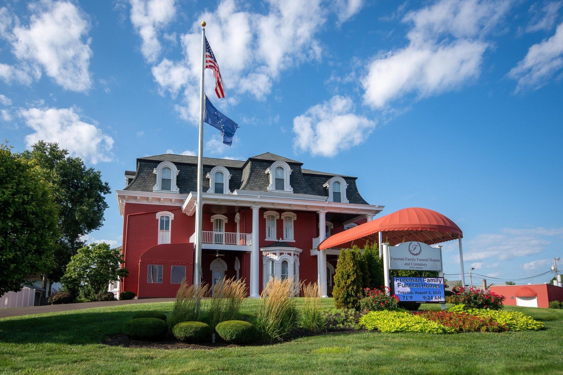 Red brick building with flag, sign, and grassy lawn under blue sky.