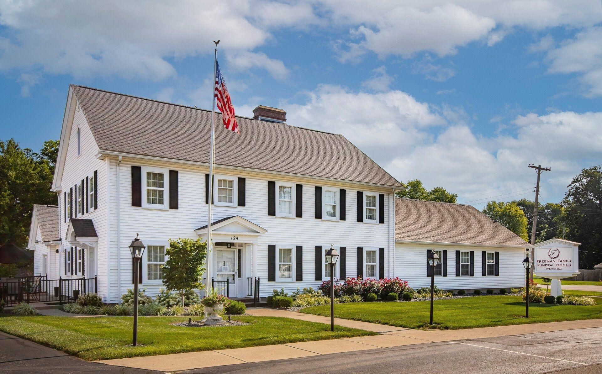 White two-story building with black shutters, American flag, and manicured lawn. 