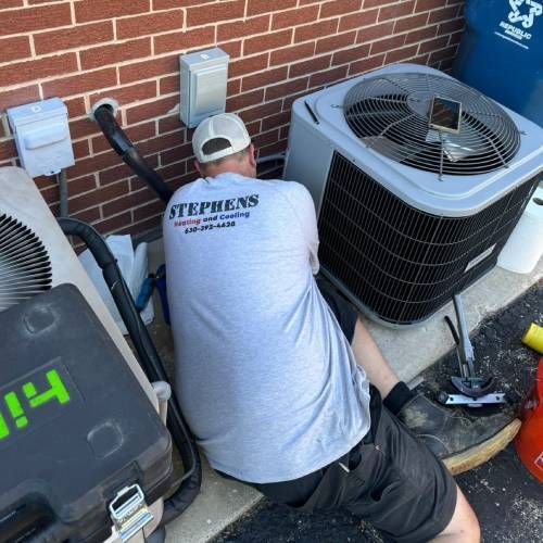 A man wearing a stephens shirt is working on an air conditioner