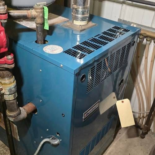 A blue boiler is sitting in a room next to pipes.