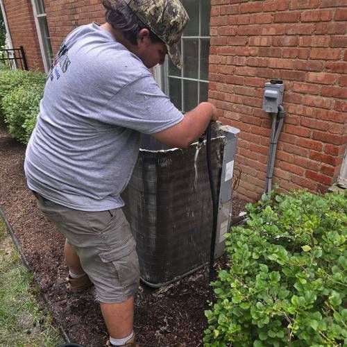 A man is working on an air conditioner outside of a brick building.