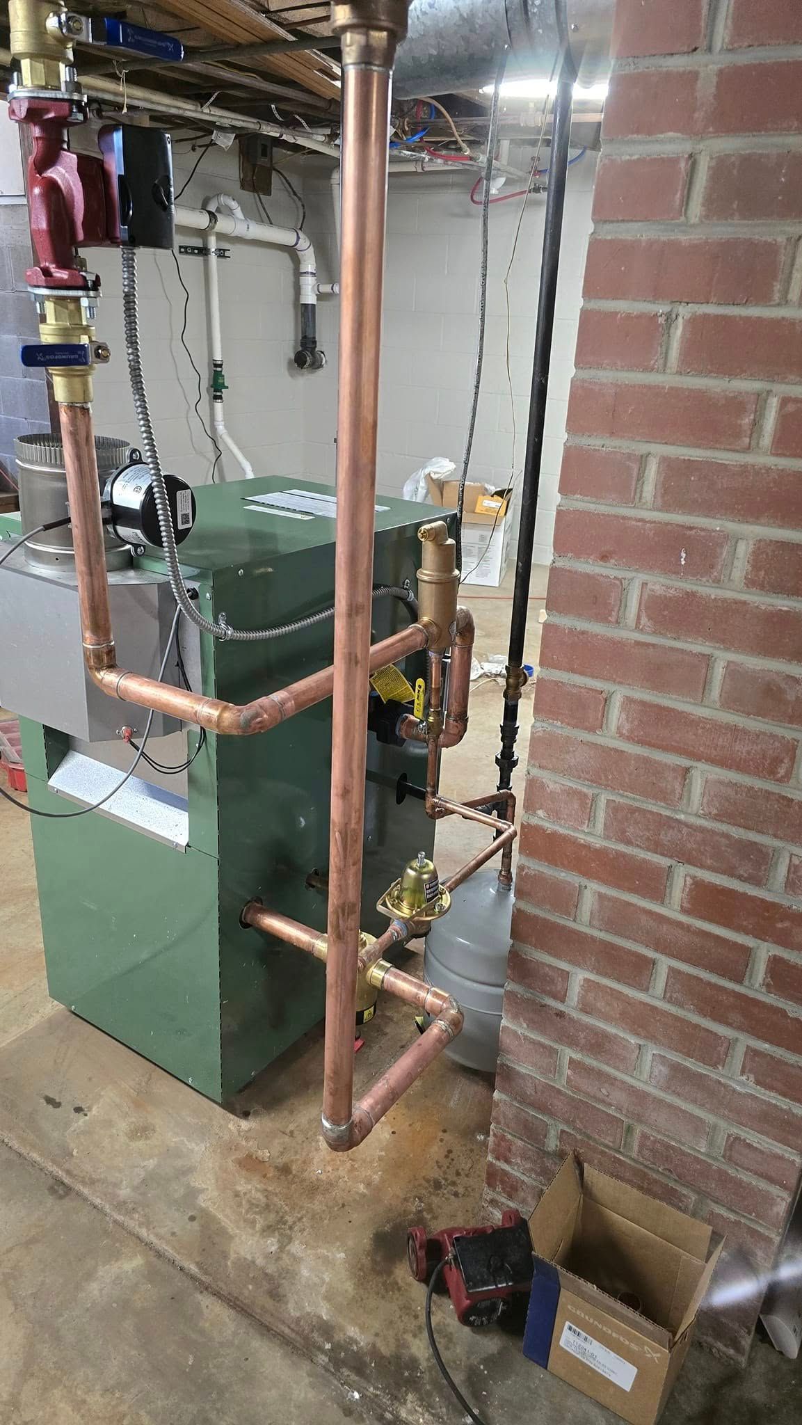A green boiler is sitting next to a brick wall in a basement.