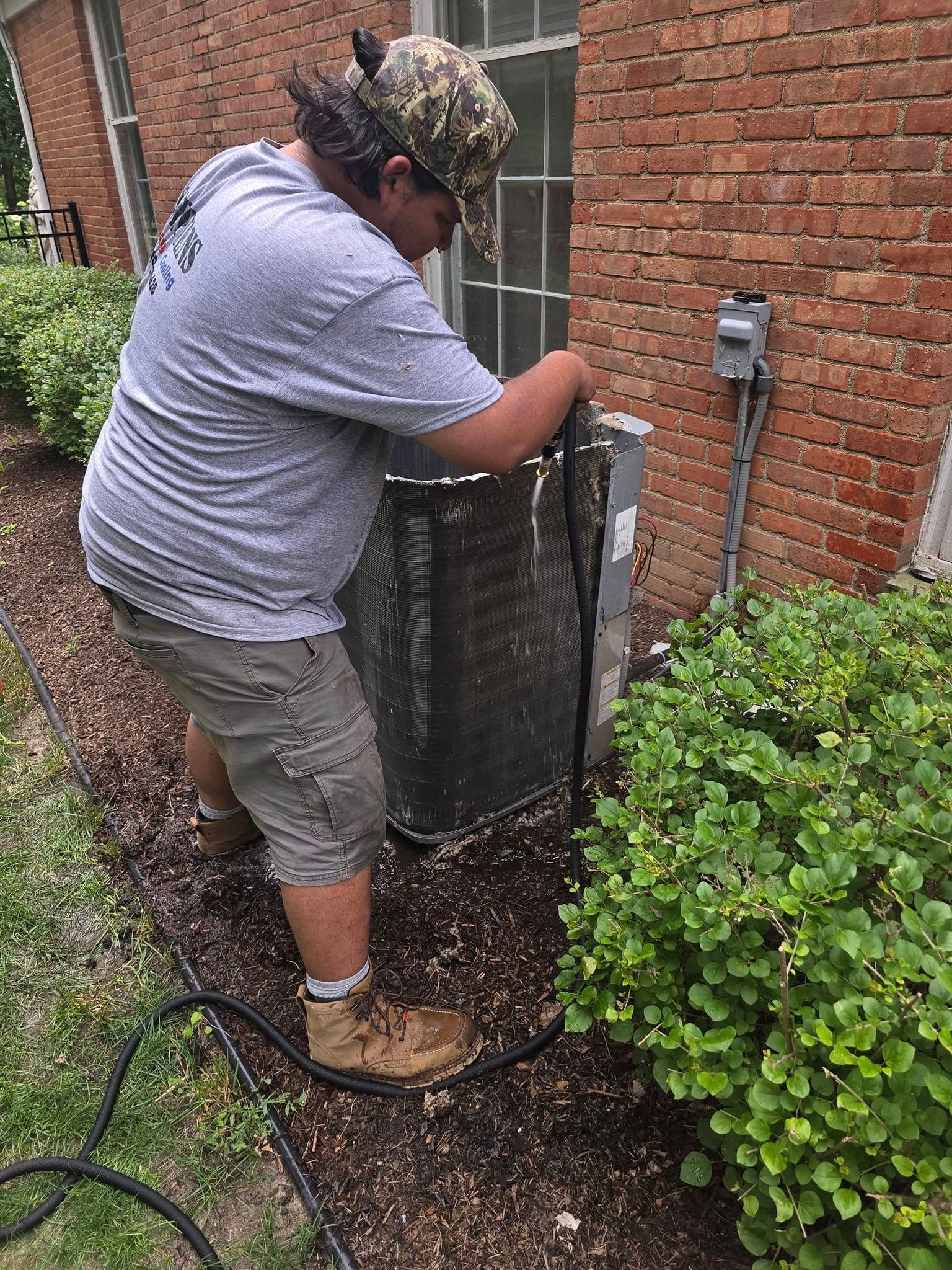 A man is working on an air conditioner outside of a brick building.