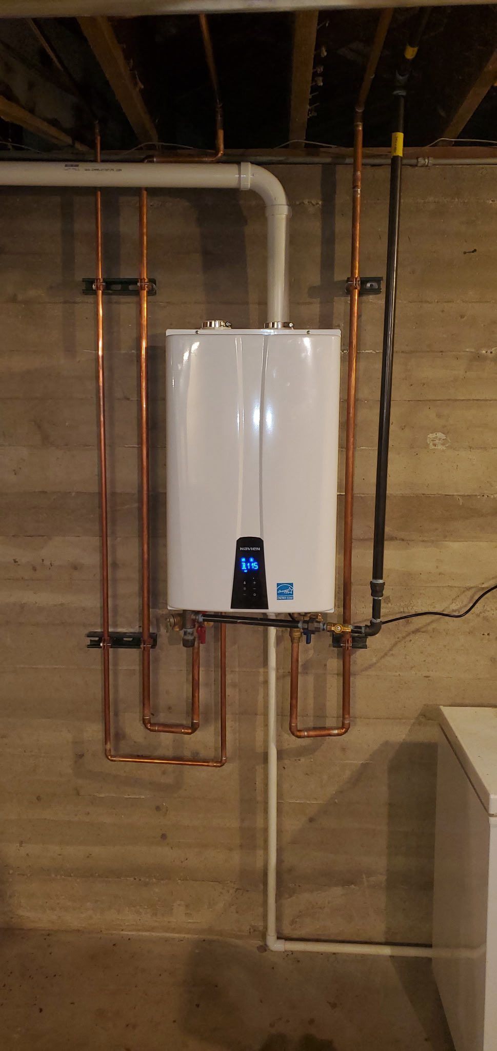 A white water heater is hanging on a wall next to copper pipes.