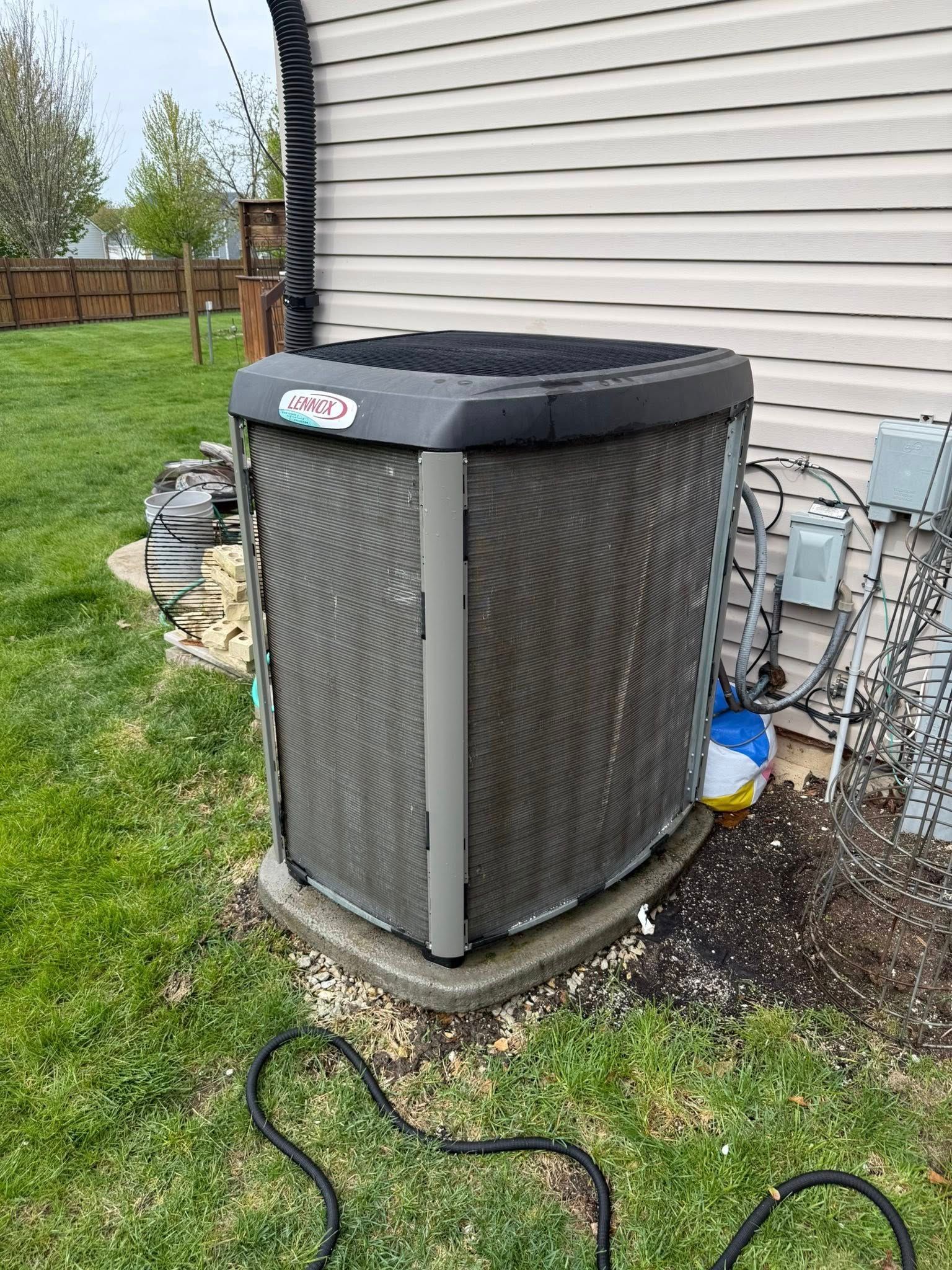 An air conditioner is sitting in the grass next to a house.