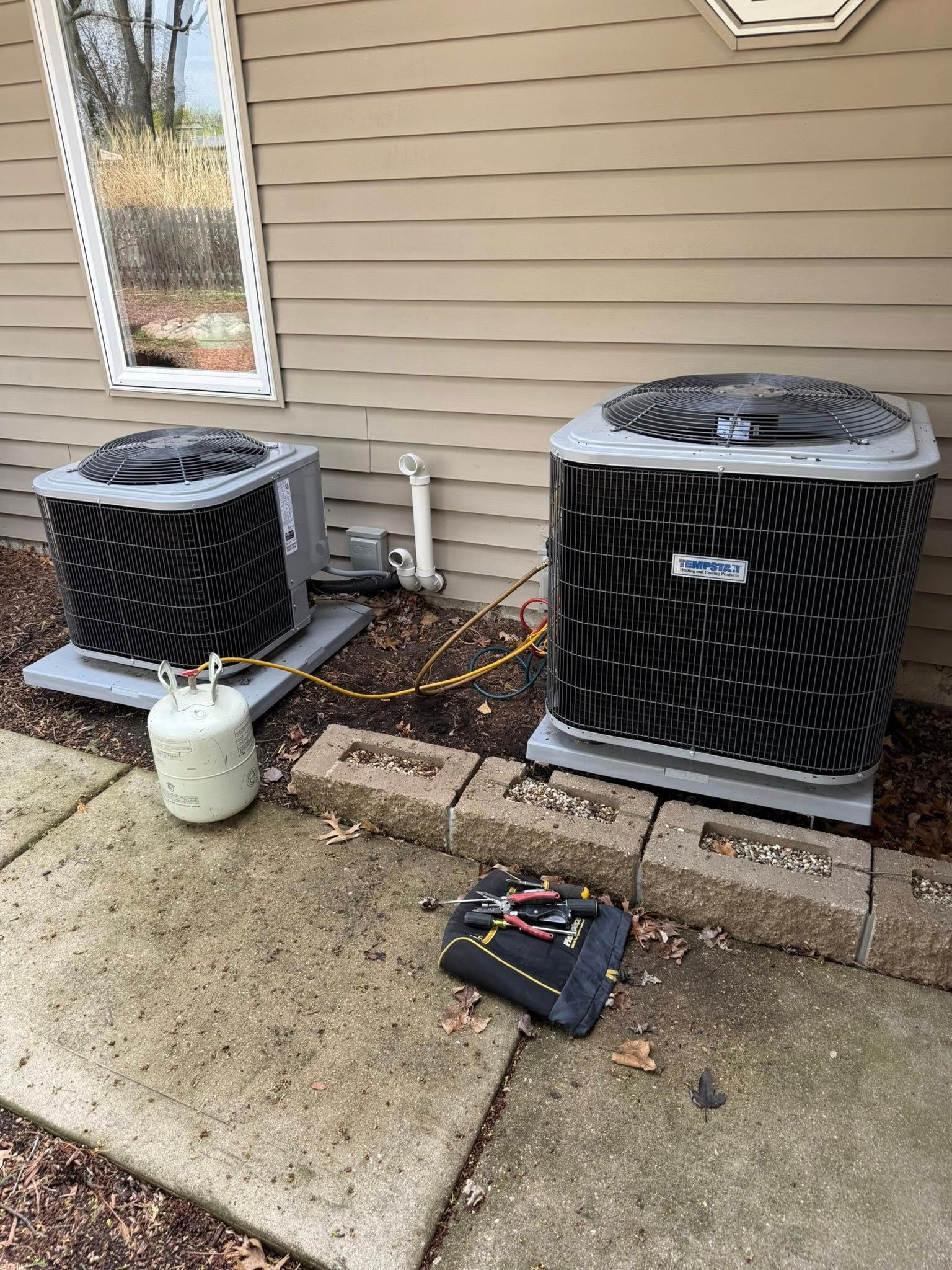 Two air conditioners are sitting next to each other on the side of a house.