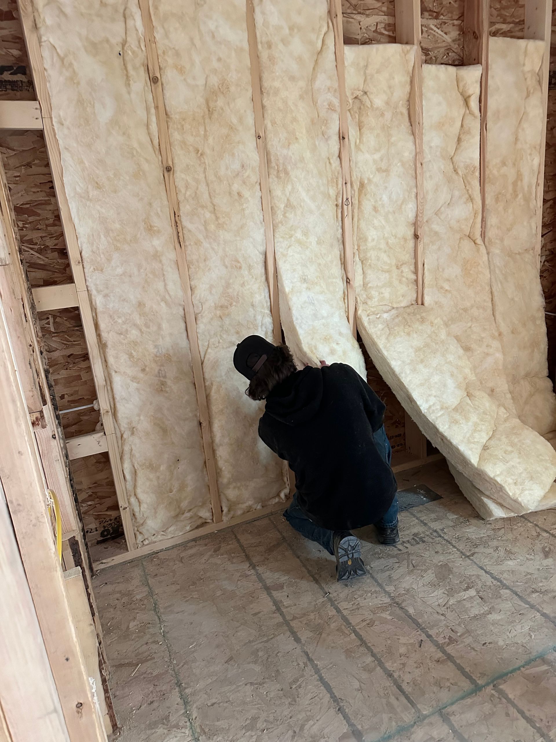 Person kneels beside insulated wall panels in a construction area with a tiled floor.