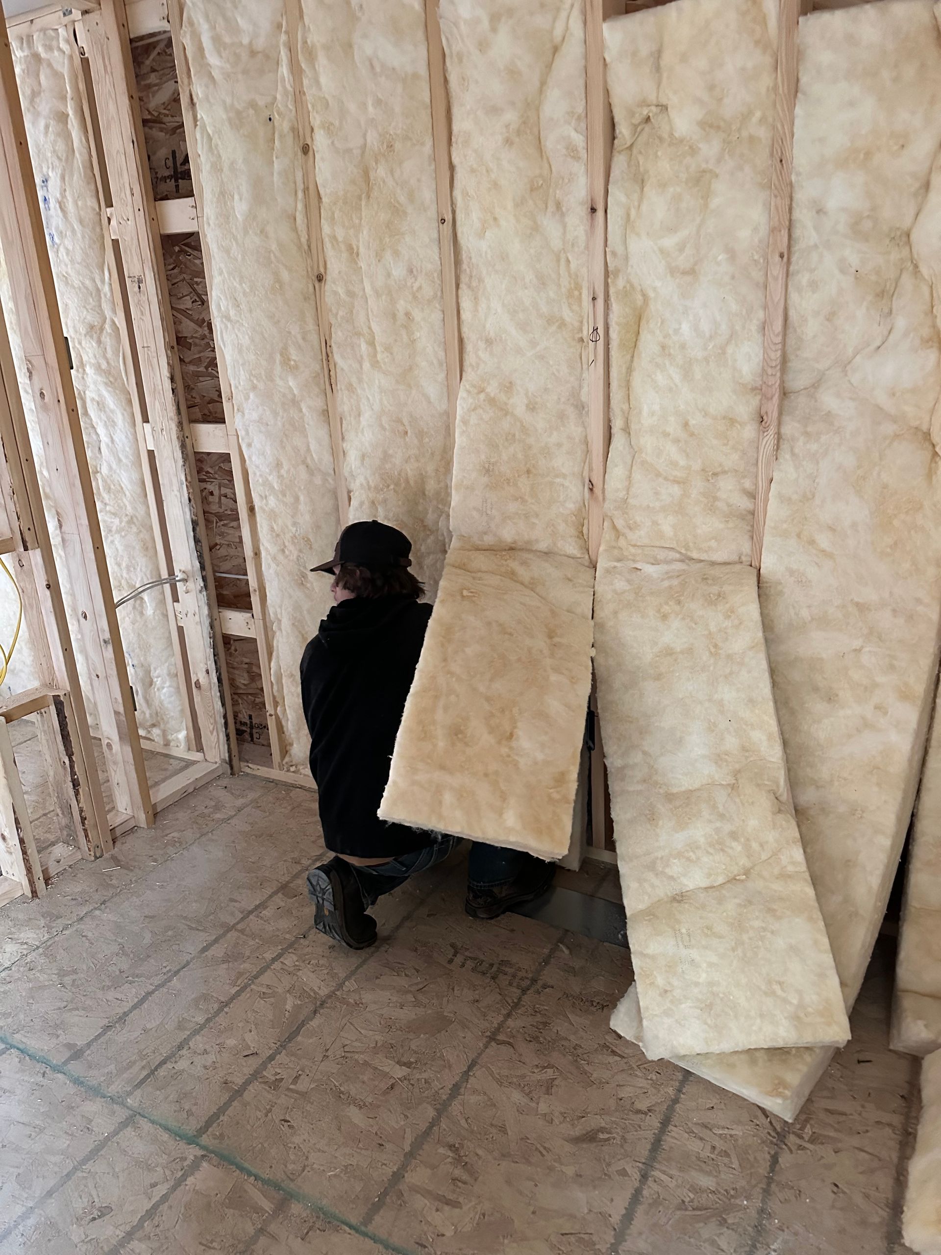 Person standing beside hanging insulation panels inside an unfinished room.