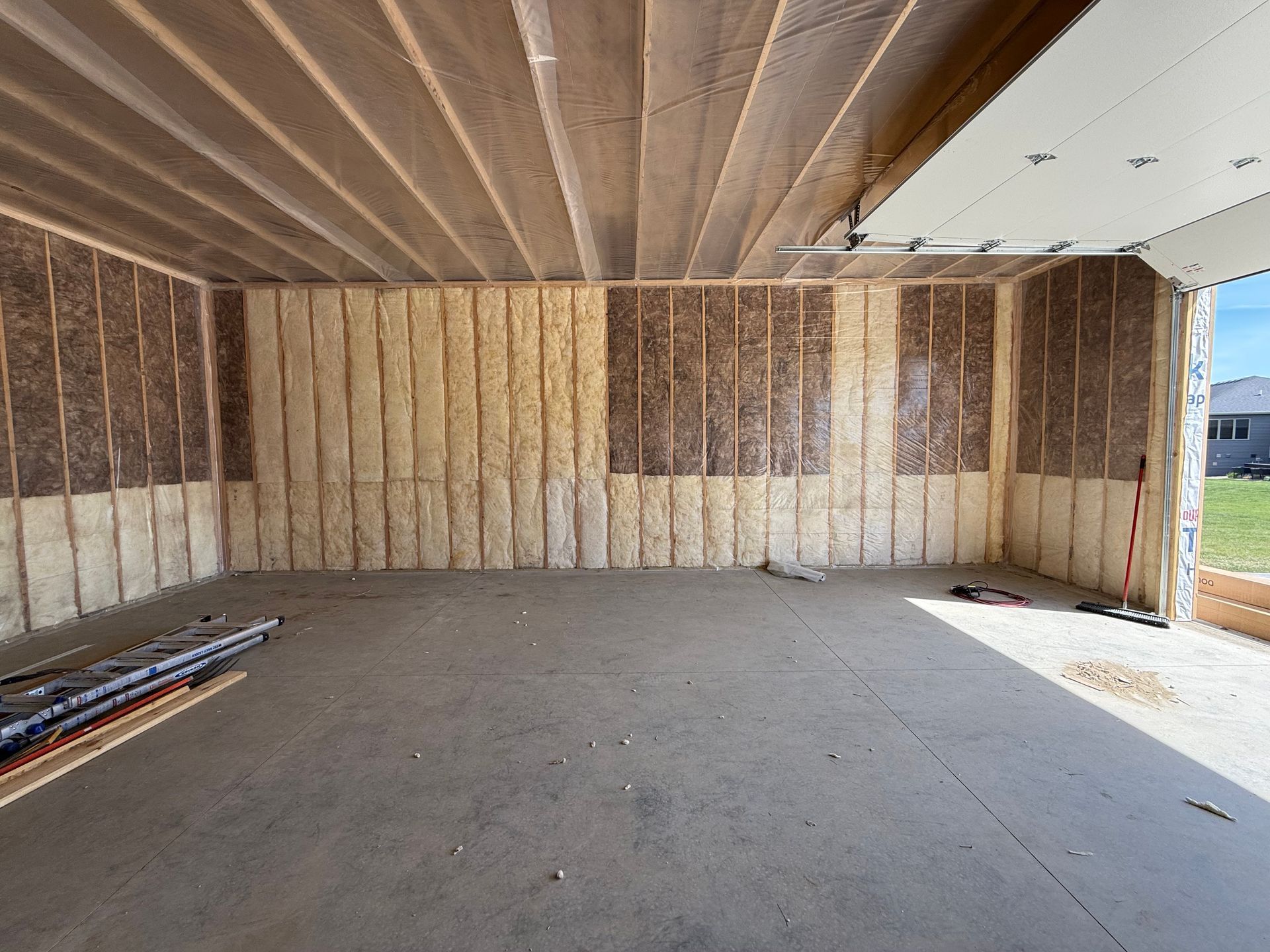 Empty unfinished room with exposed insulation, concrete floor, and daylight from a doorway on the right.