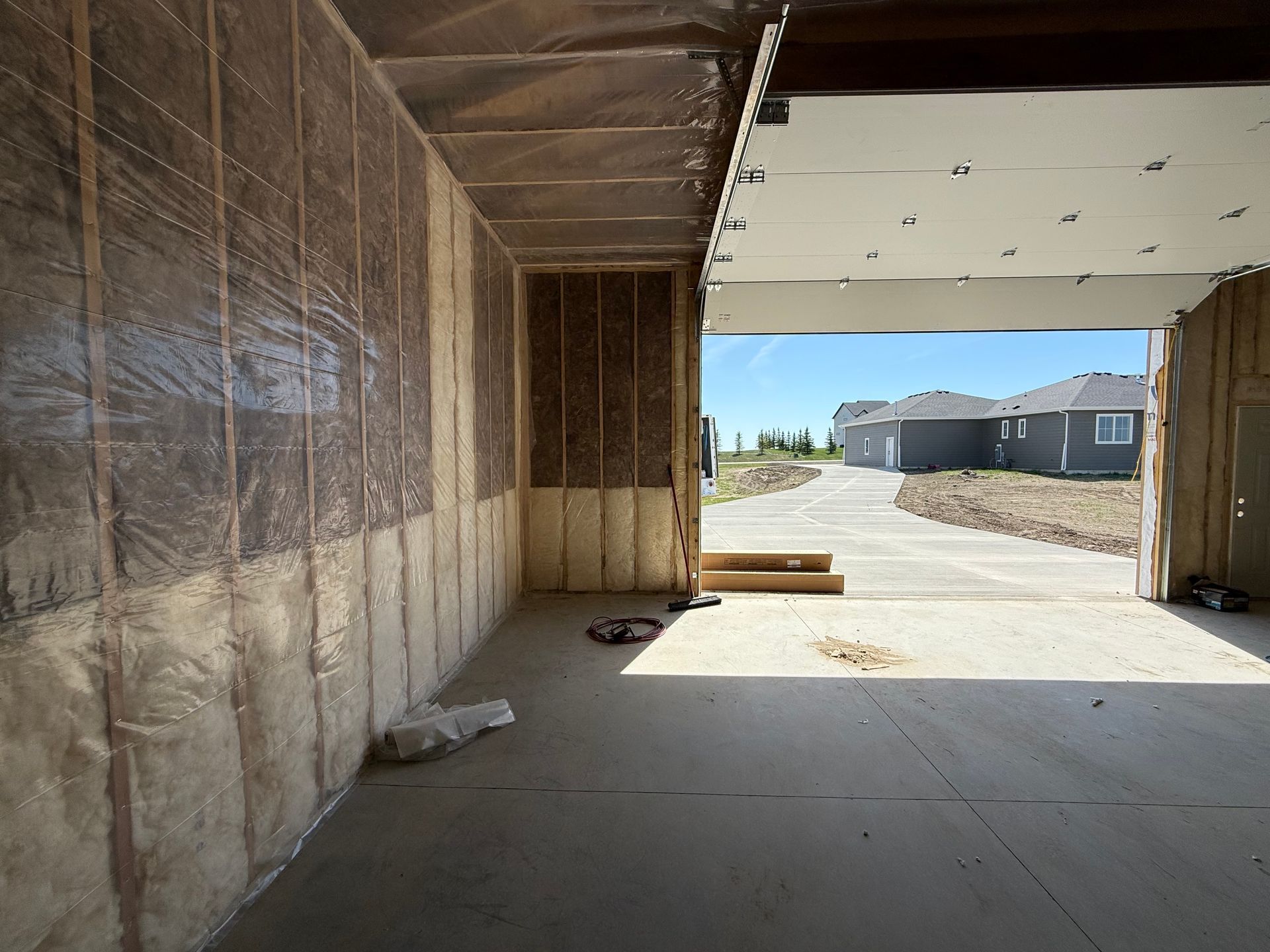 Unfinished building interior with exposed insulation, opening to a sunny construction site outside