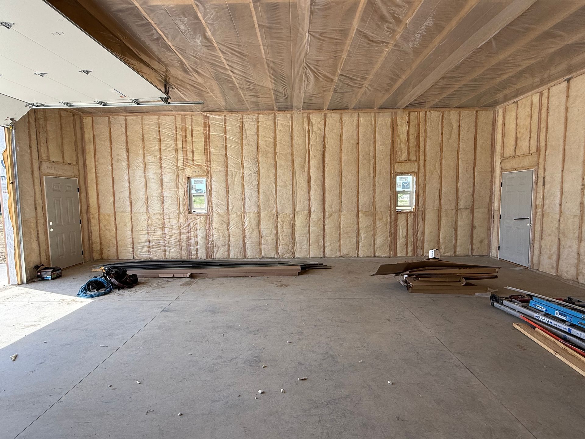 Empty unfinished room with exposed wooden walls, two small windows, and construction materials on the floor