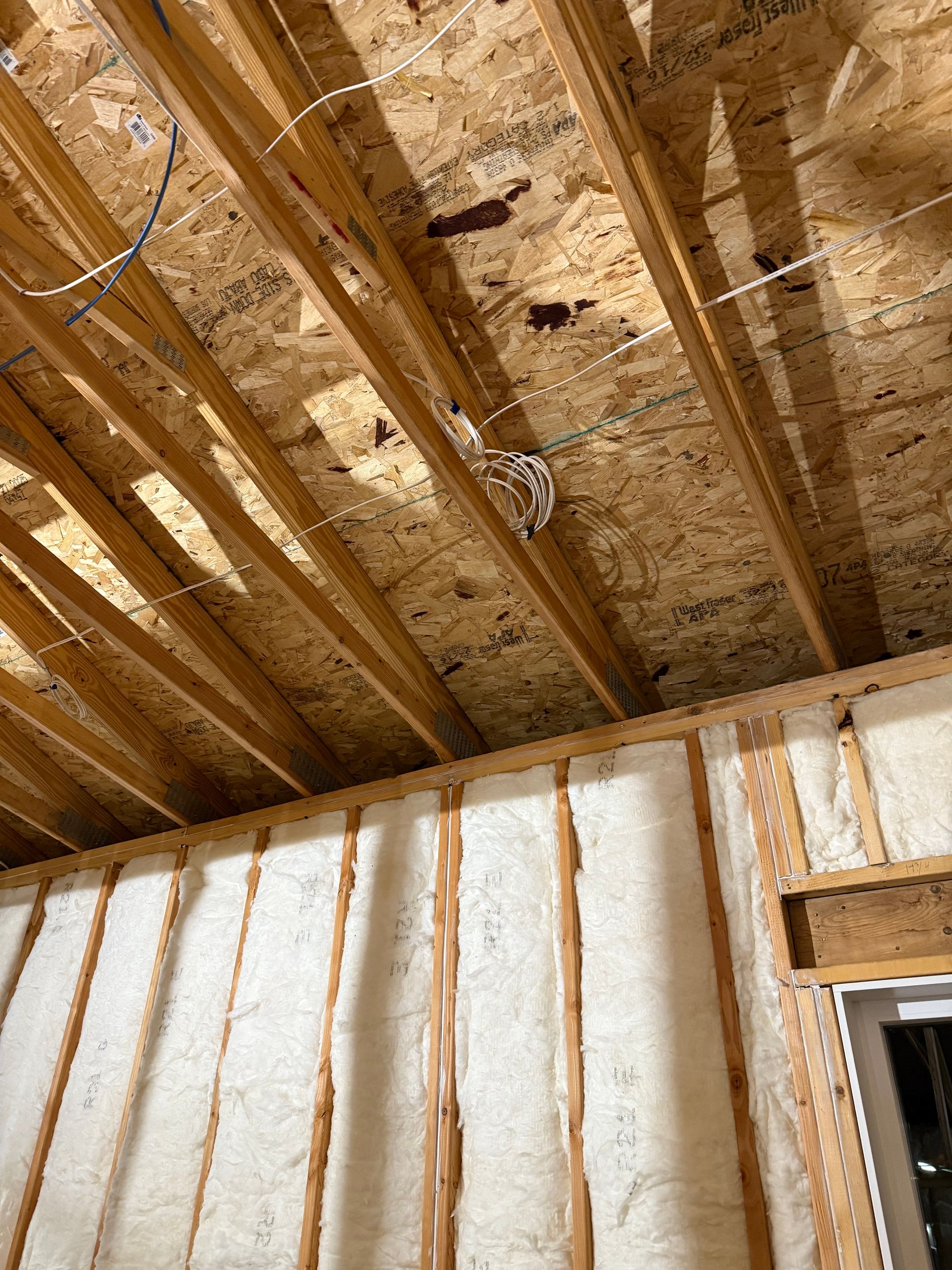 Exposed attic ceiling joists and OSB sheathing above unfinished insulated wall framing.