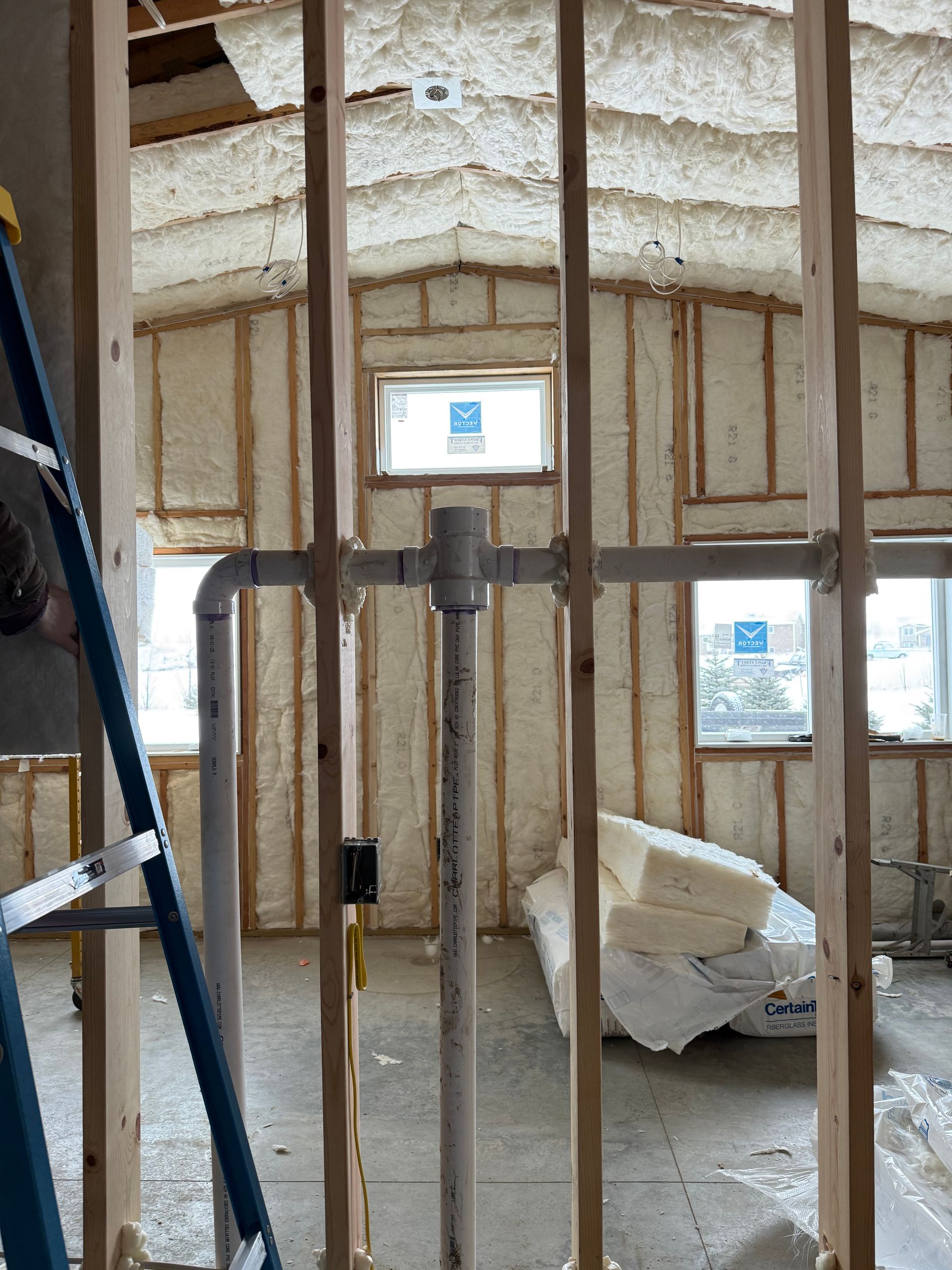 Exposed wall framing in an unfinished room with spray foam insulation and a small window opening.