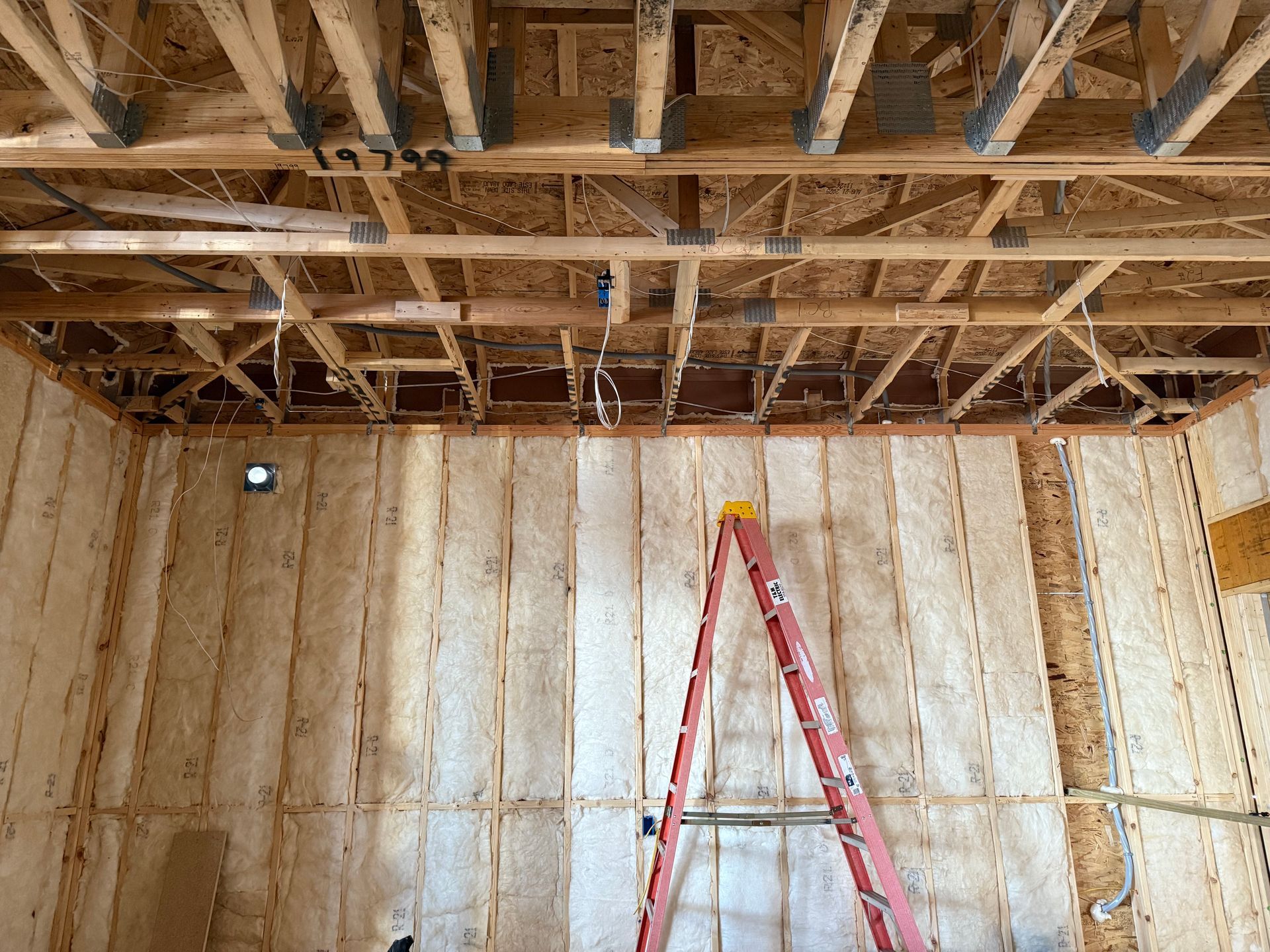 Partially finished room with exposed ceiling beams and a red ladder against unfinished walls