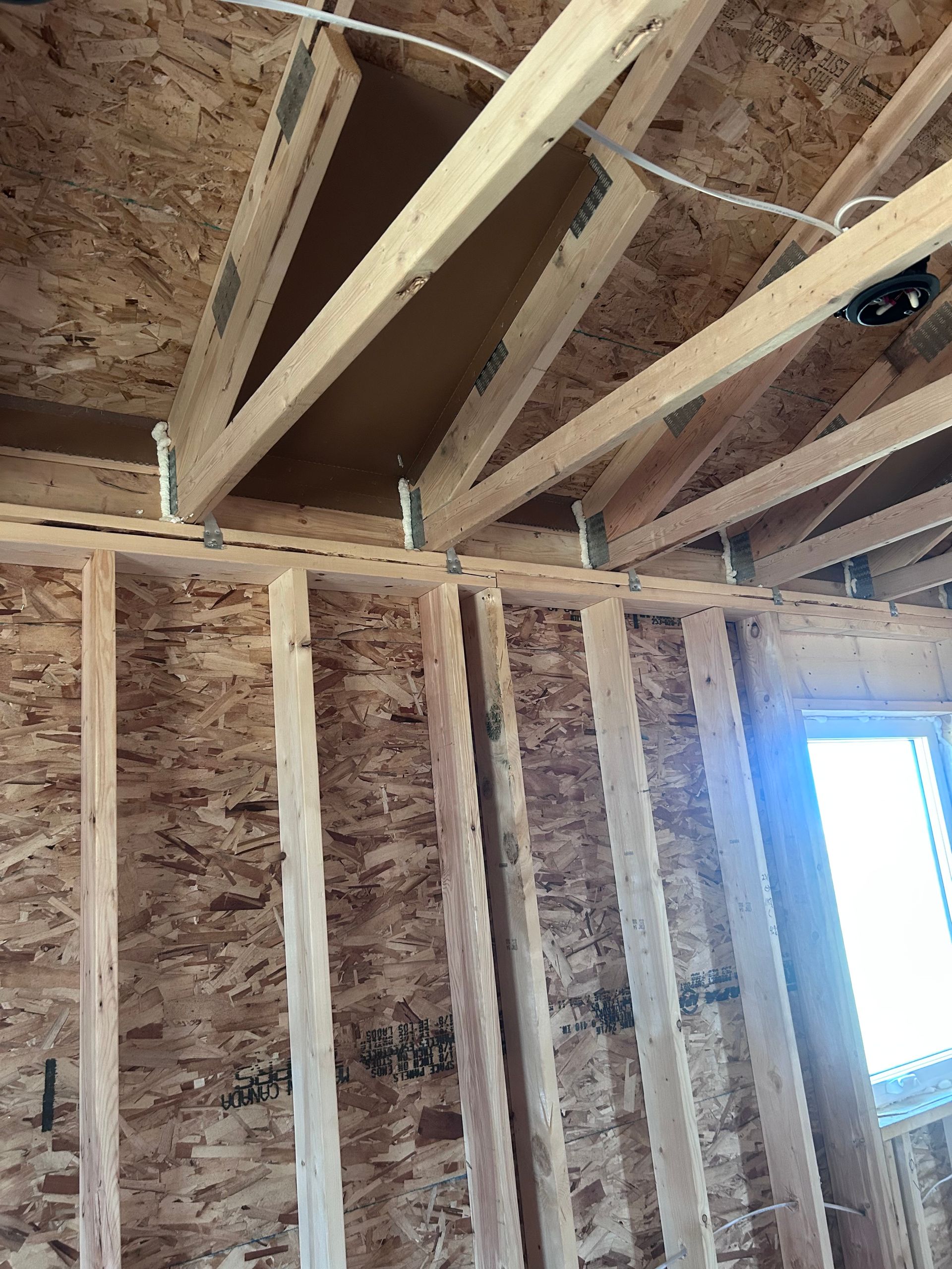 Unfinished room with exposed wooden wall studs, roof trusses, and a bright window opening.