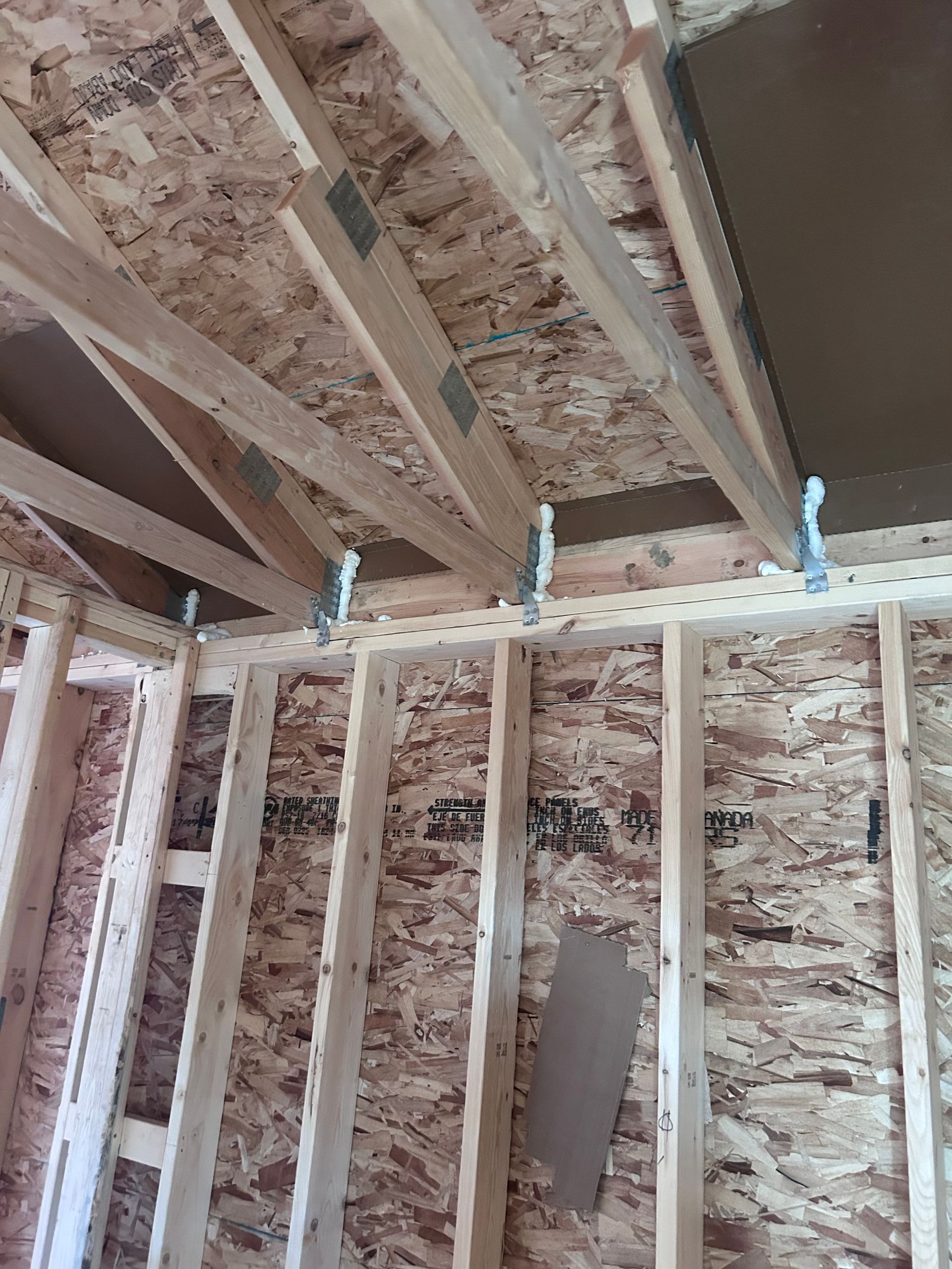Exposed wooden wall framing and ceiling joists in an unfinished interior under construction.