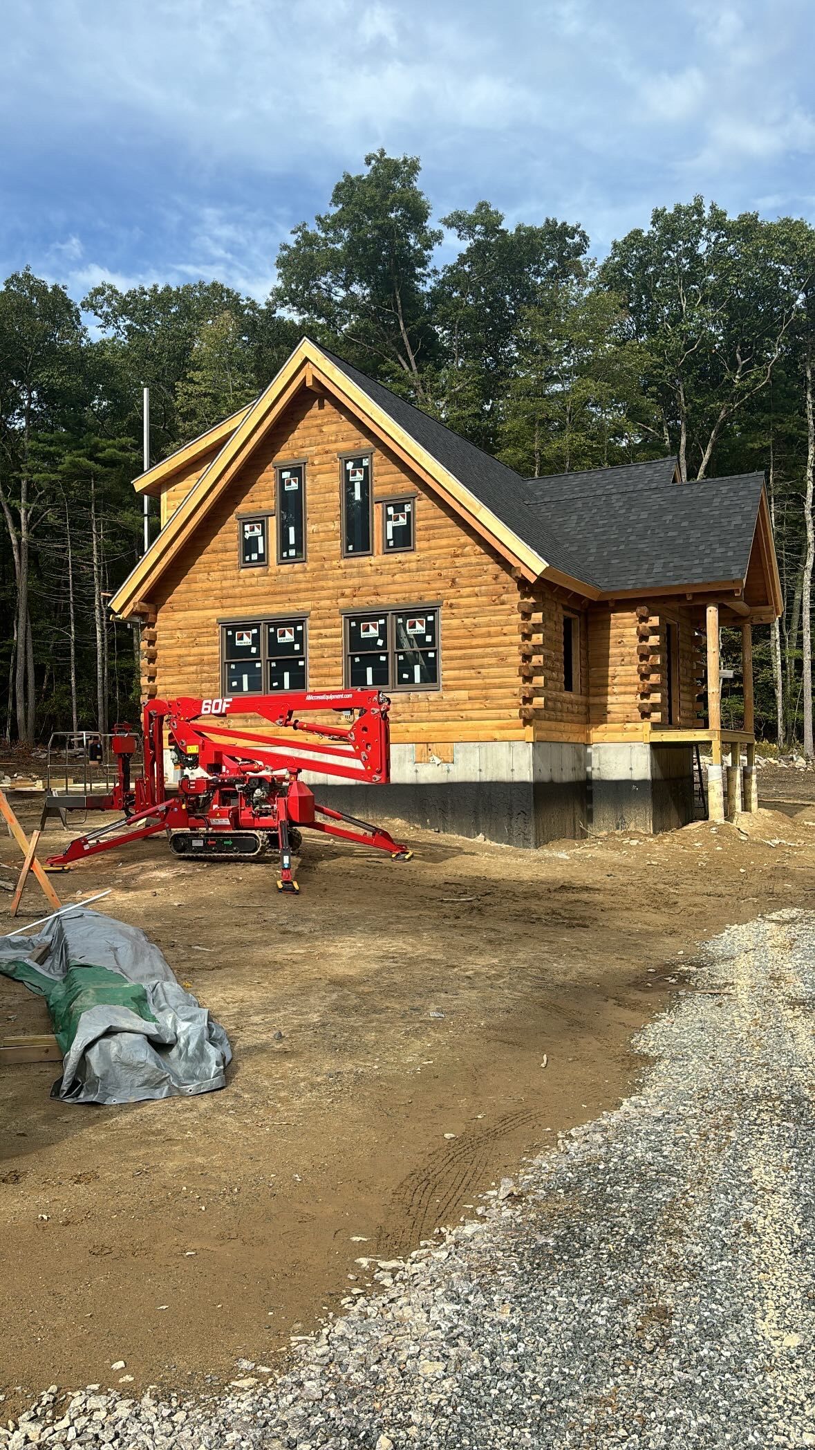 A log cabin is being built in the woods with a crane in front of it.