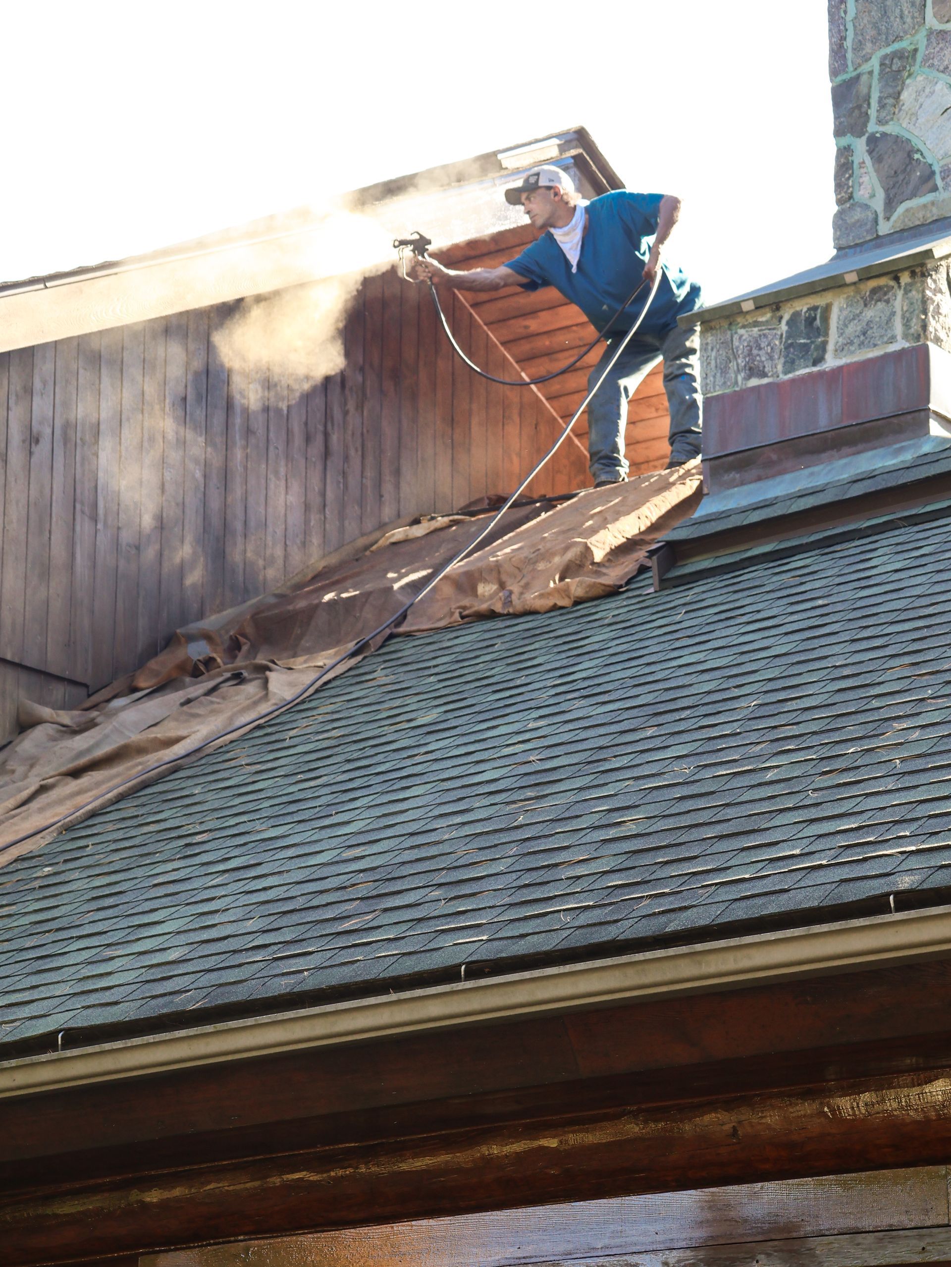 A man is standing on top of a roof spraying paint