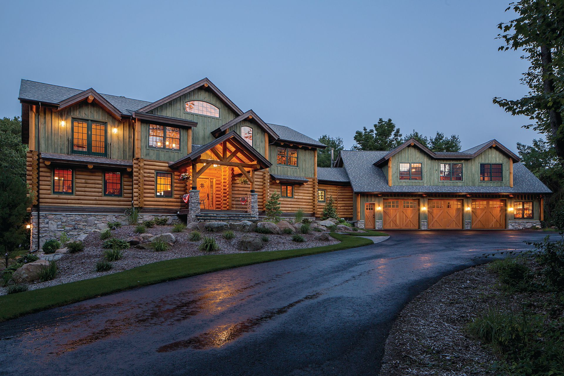 A large log home with a driveway leading to it is lit up at night.