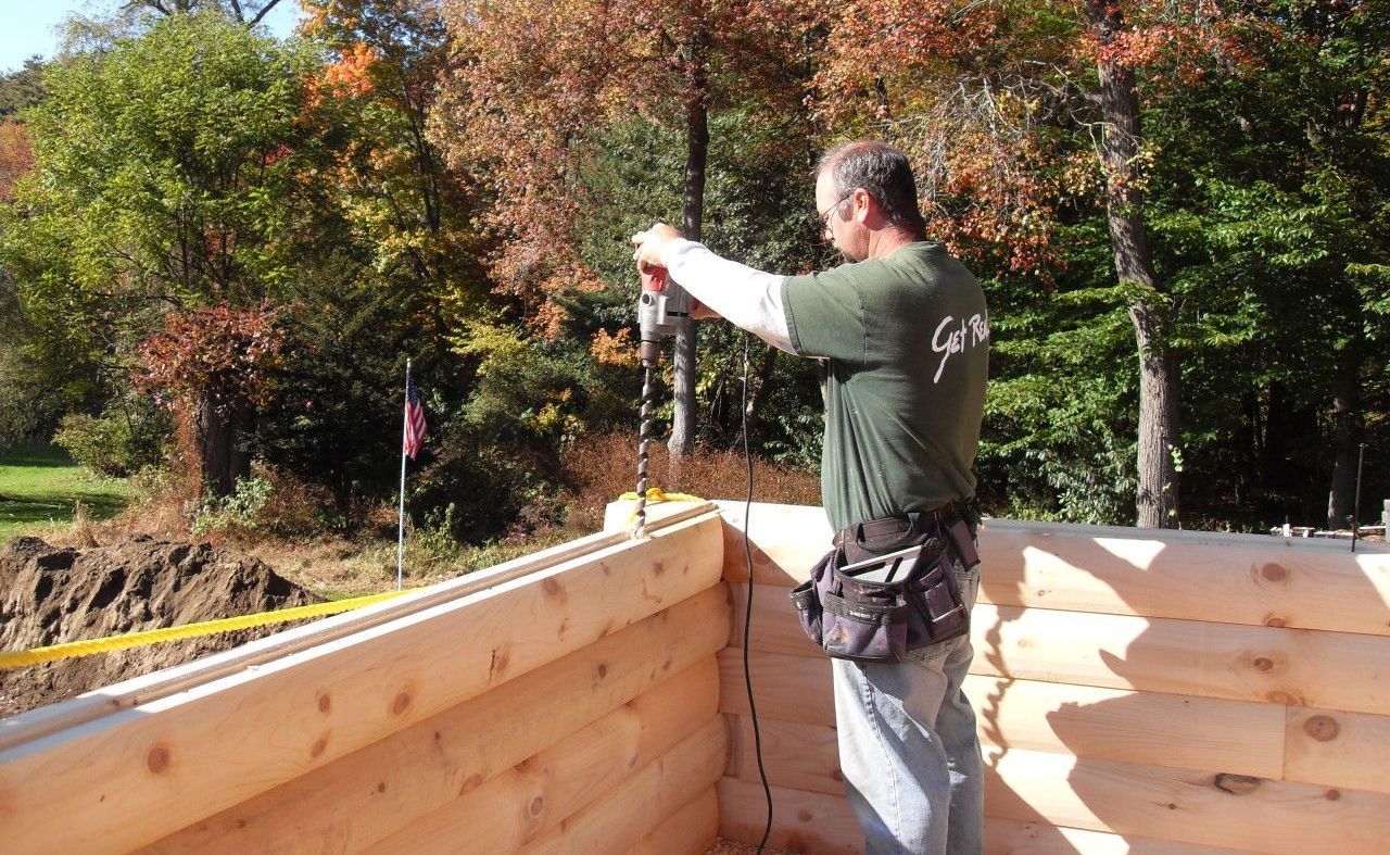 A man in a green shirt is working on a log cabin