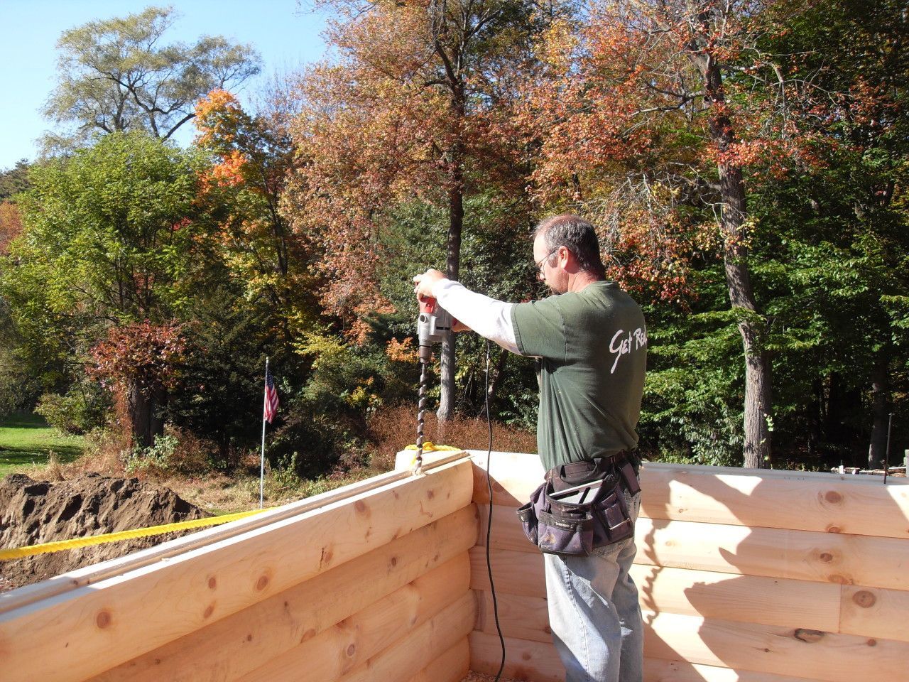 A man in a green shirt is working on a log cabin