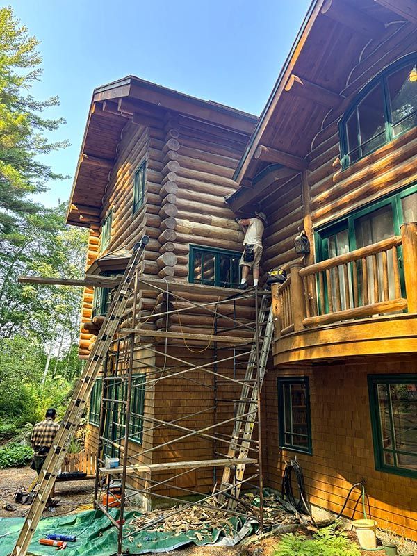 A man is painting the side of a log cabin.