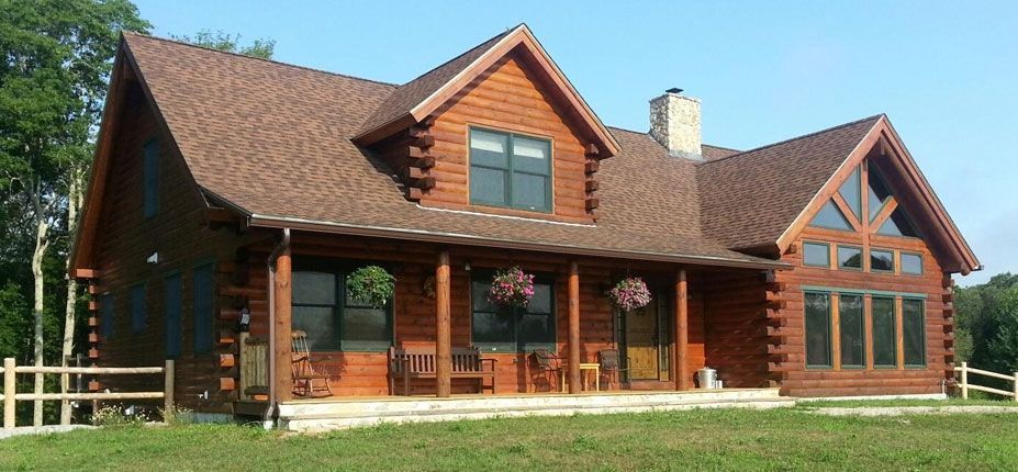 A large log cabin with a porch and a fence in front of it