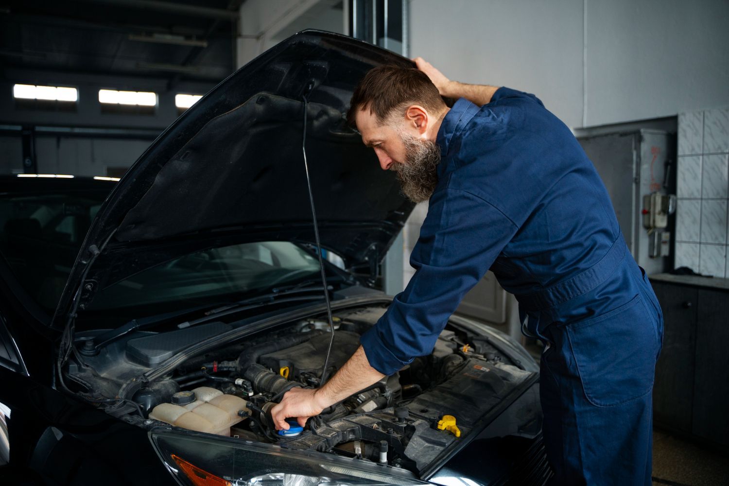 A man is working on the engine of a car in a garage.