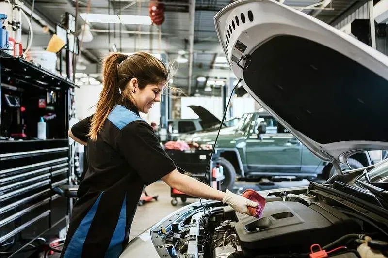 Female mechanic inspecting car engine in auto shop.