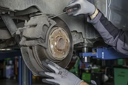 Mechanic repairing a car disc brake system with a screwdriver.
