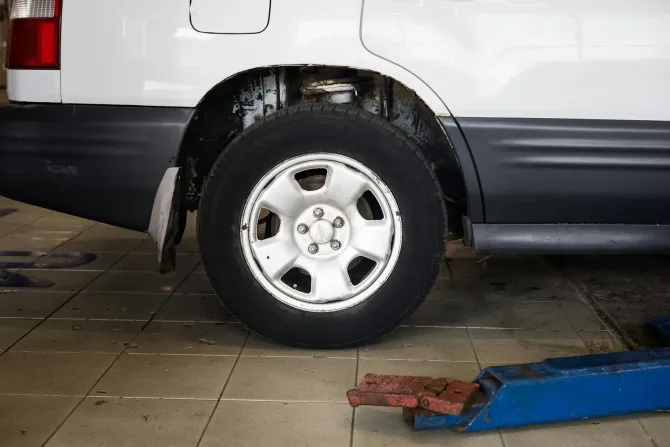 A close-up view of the rear wheel and undercarriage of a white vehicle lifted on a blue metal mechanic's shop lift.