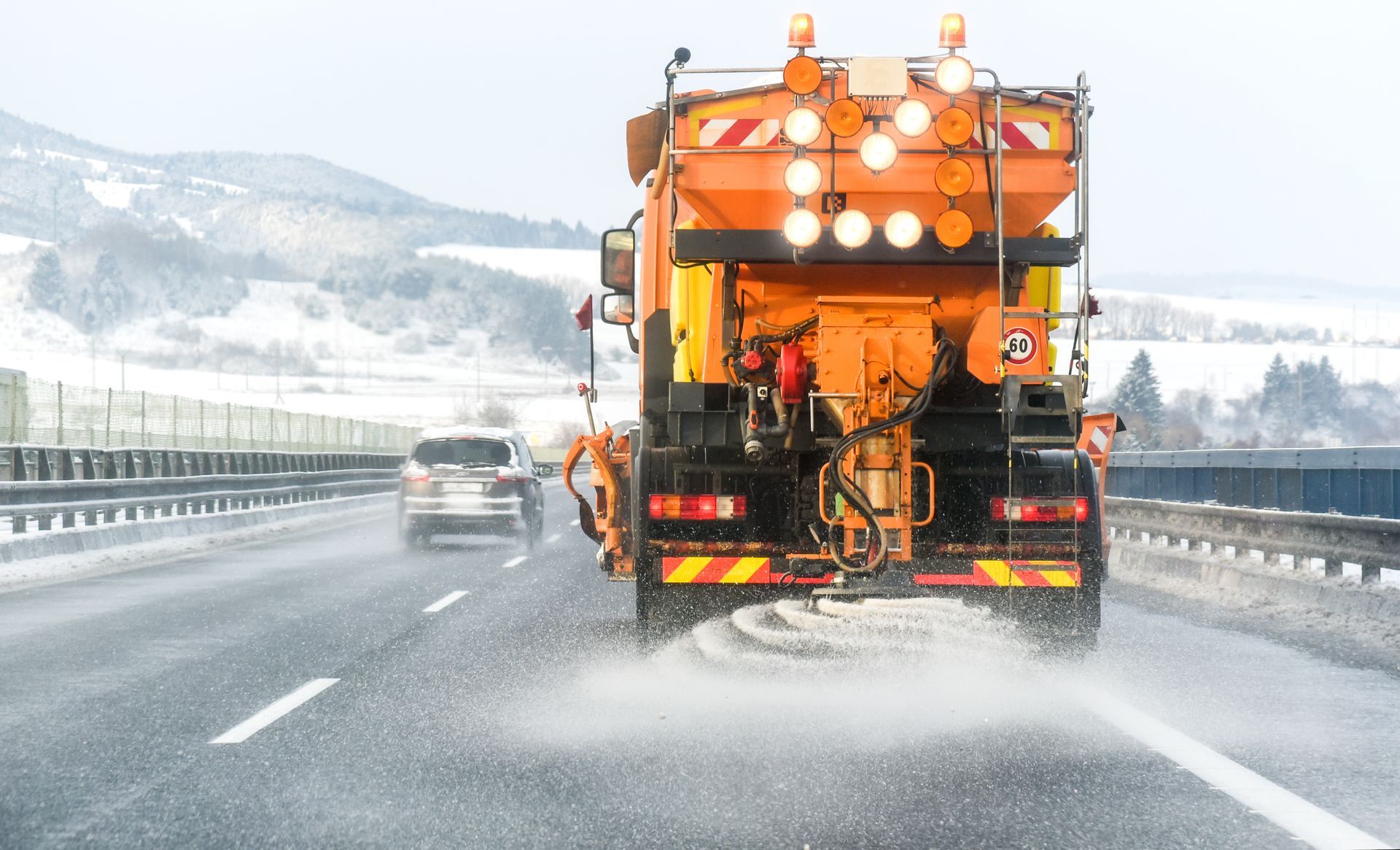 A snow plow equipped with a salt spreader in action, clearing and de-icing a highway during winter.