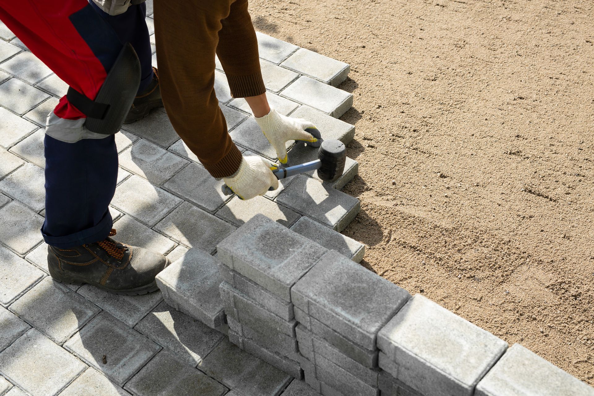 Worker's hands carefully aligning and securing concrete blocks and paving slabs using a rubber hammer during installation.